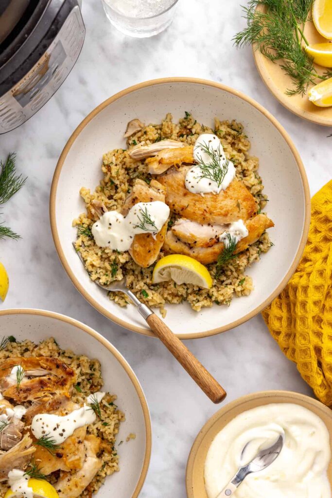 Overhead view of Instant Pot Greek lemon chicken and rice topped with lemon yogurt sauce and fresh herbs.