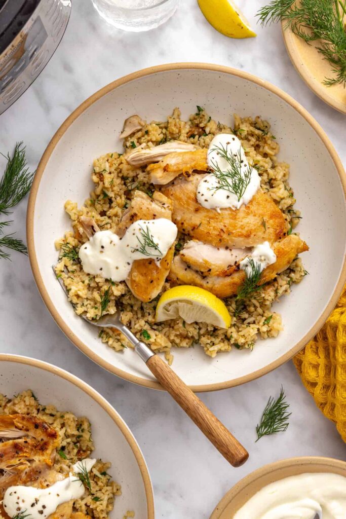 Instant Pot chicken and rice with fresh dill, parsley, lemon, and dollops of Greek yogurt sauce.