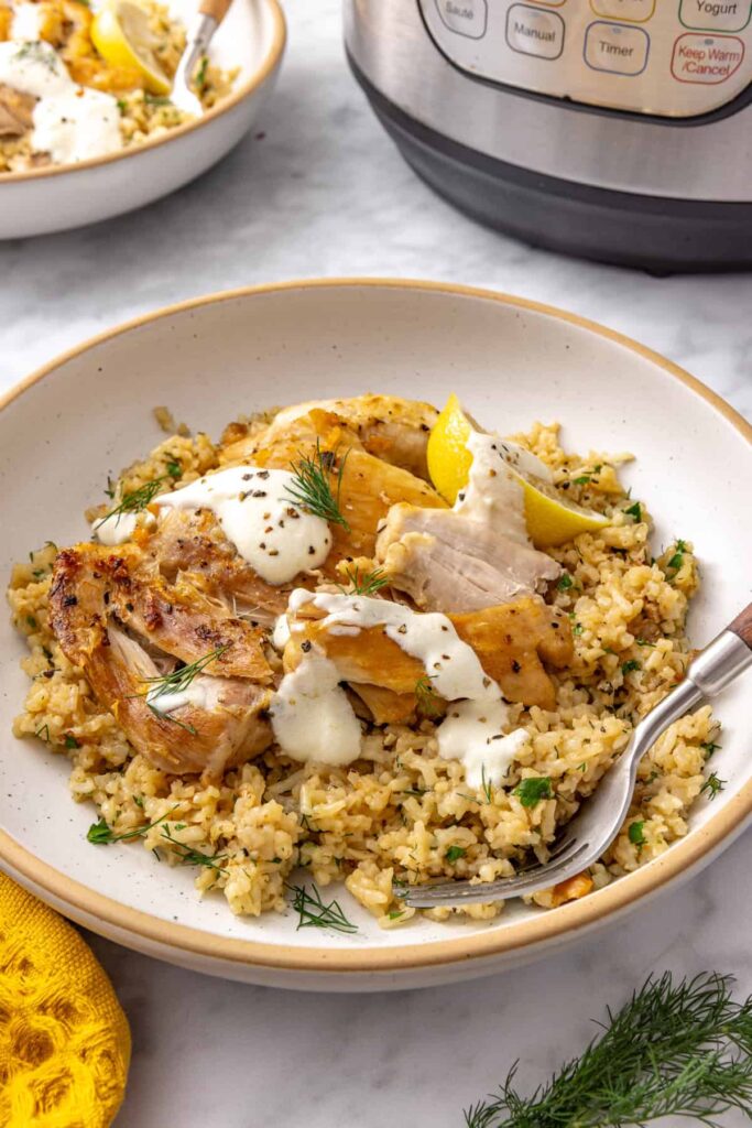 Side view of Instant Pot Greek lemon chicken served over fluffy lemon herb rice with creamy yogurt sauce.