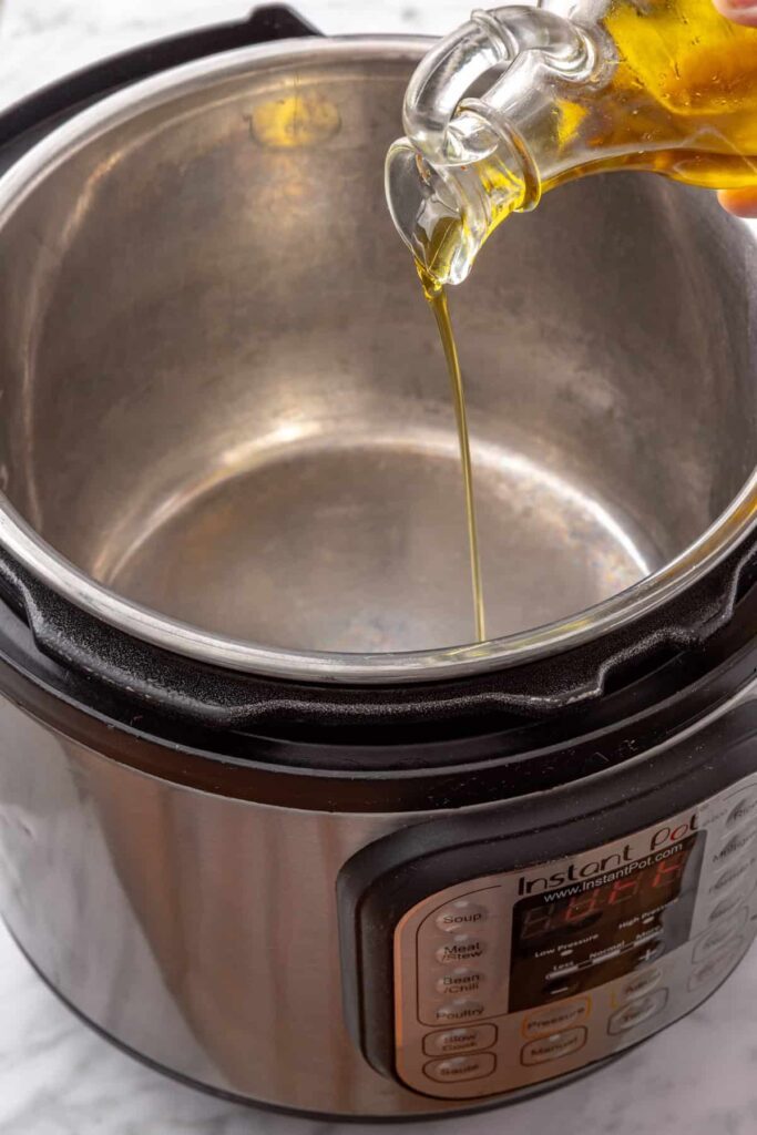 pouring olive oil into the Instant Pot before searing chicken thighs