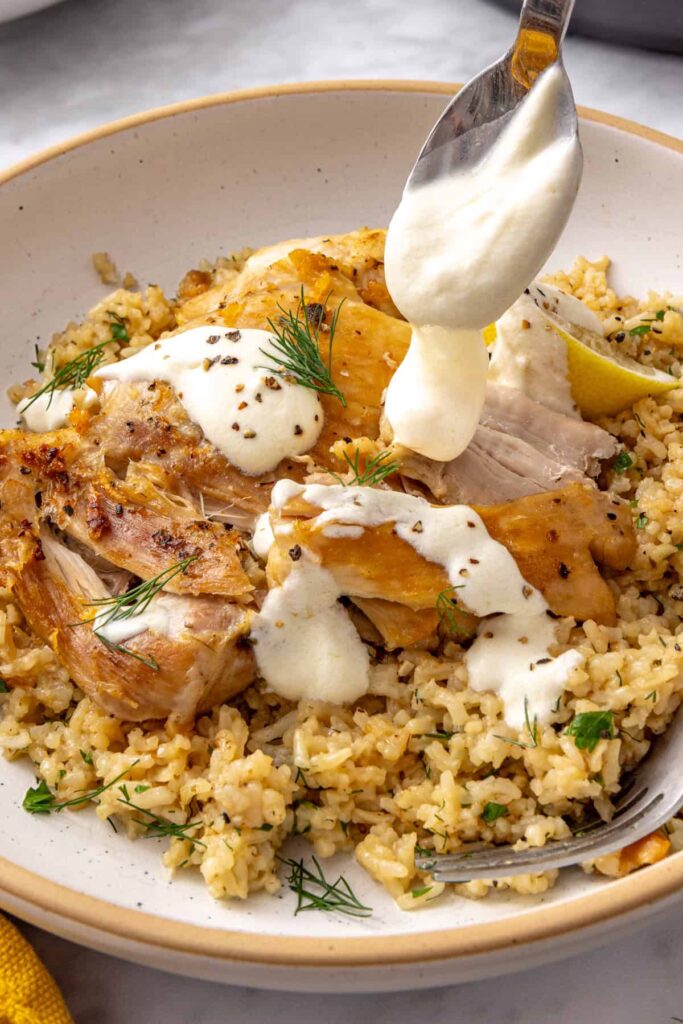 Spoon drizzling creamy lemon yogurt sauce over Instant Pot Greek lemon chicken and rice.