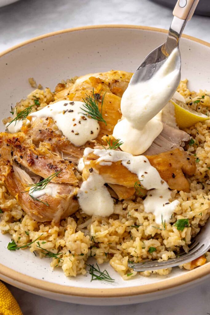 Lemon garlic yogurt sauce being spooned over tender chicken thighs and fluffy herb rice.