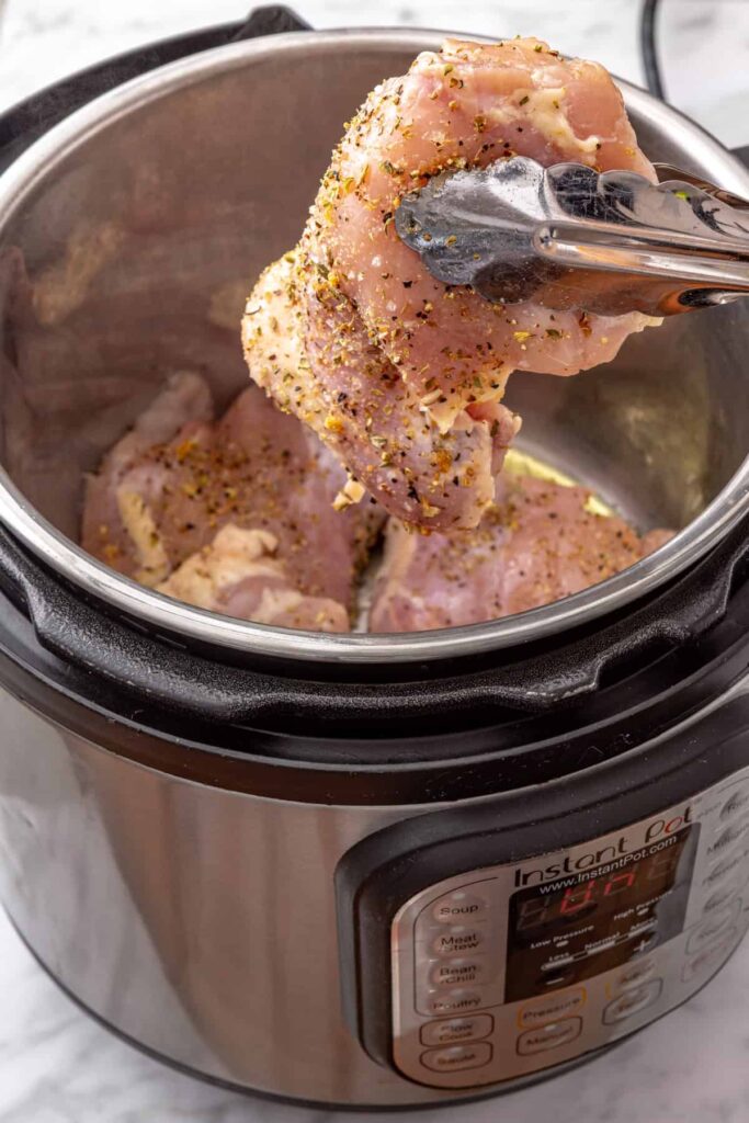 Chicken thighs searing in olive oil in the Instant Pot before cooking with lemon herb rice.