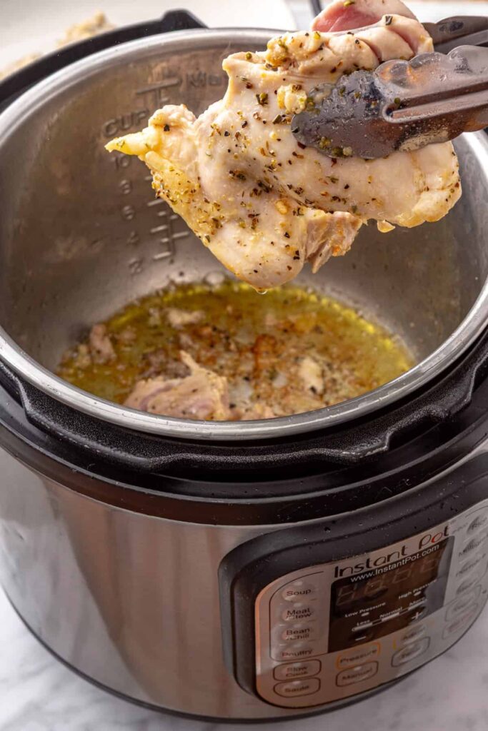 Golden-brown chicken thighs being seared on both sides using the Instant Pot Sauté setting.