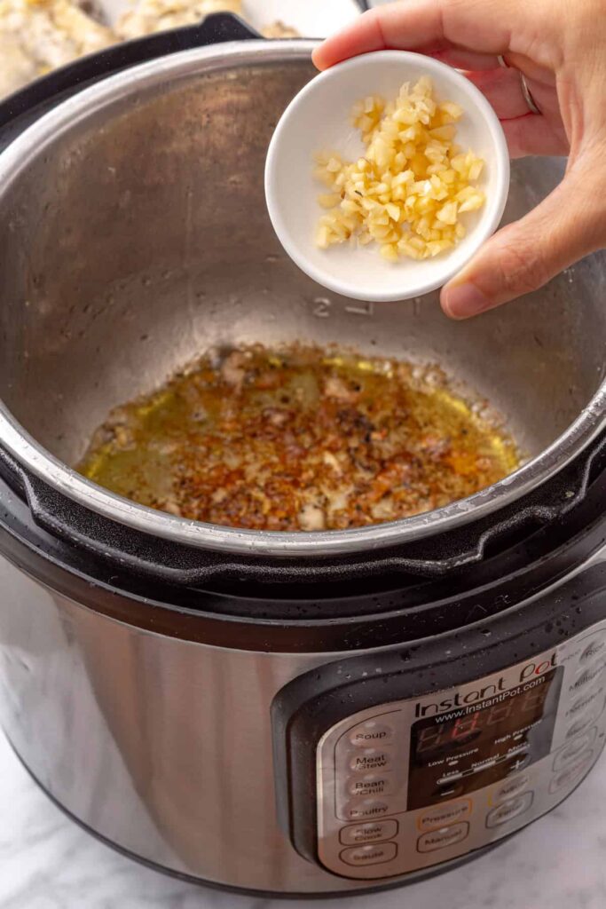 Minced garlic sautéing in olive oil in the Instant Pot after searing the chicken thighs.