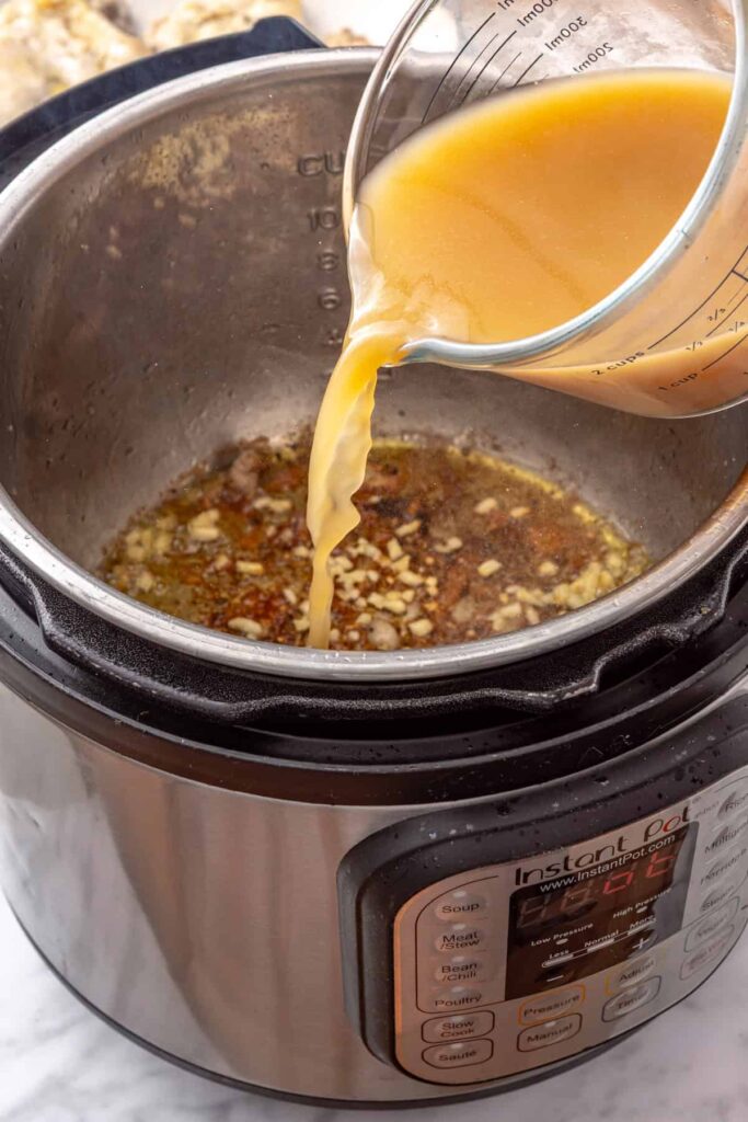 Chicken broth being poured into the Instant Pot to deglaze the pot after sautéing garlic.