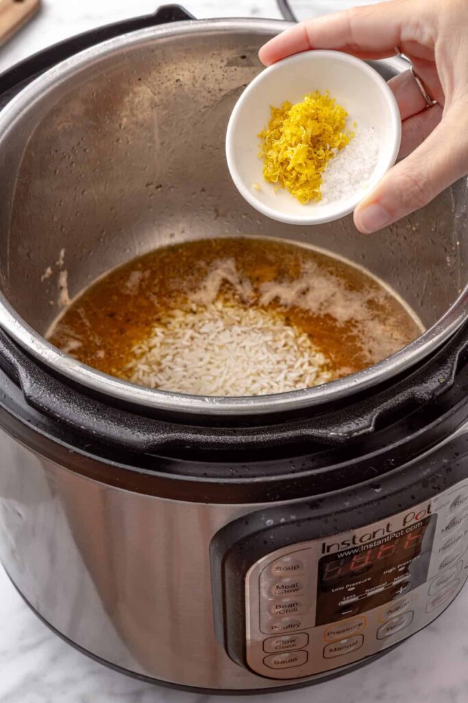 Uncooked rice, lemon zest, and seasoned chicken broth prepared for Instant Pot Greek lemon chicken and rice.
