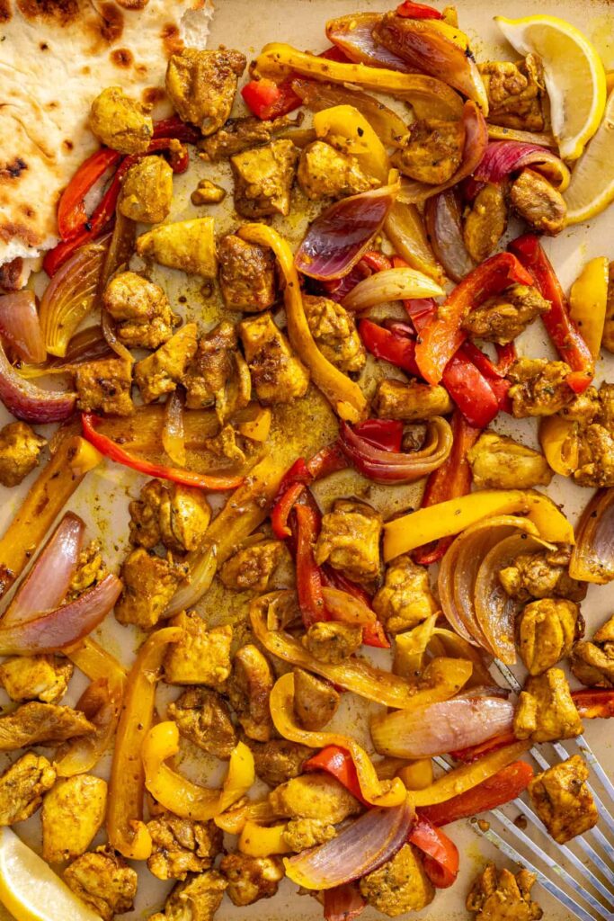 Chicken shawarma and roasted vegetables ready to serve, with pita bread alongside the sheet pan.