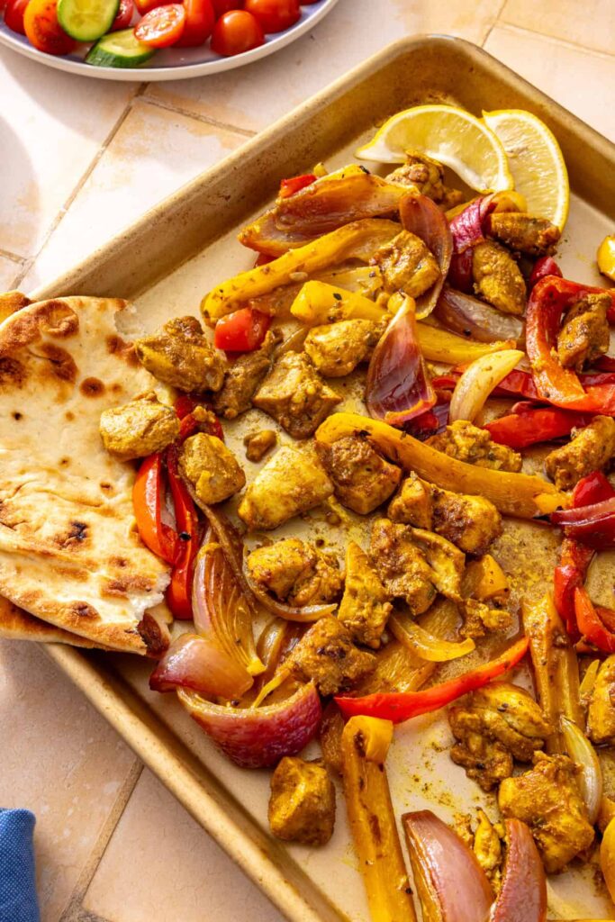 Homemade roasted chicken shawarma with colorful vegetables and pita bread, ready to assemble into bowls.