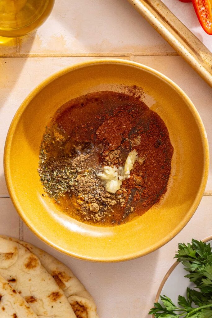 Olive oil, lemon juice, garlic, cumin, smoked paprika, coriander, oregano, turmeric, salt, and pepper ready to be whisked together for chicken shawarma.