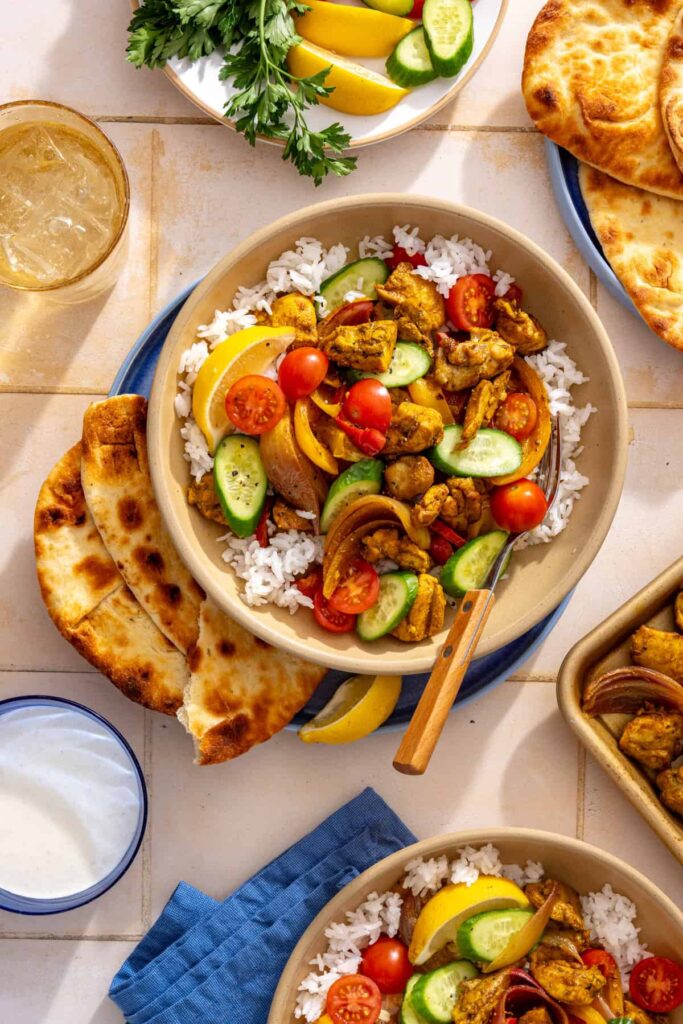 Overhead chicken shawarma bowl with basmati rice, roasted peppers and onion, cucumber, cherry tomatoes, and a lemon wedge.