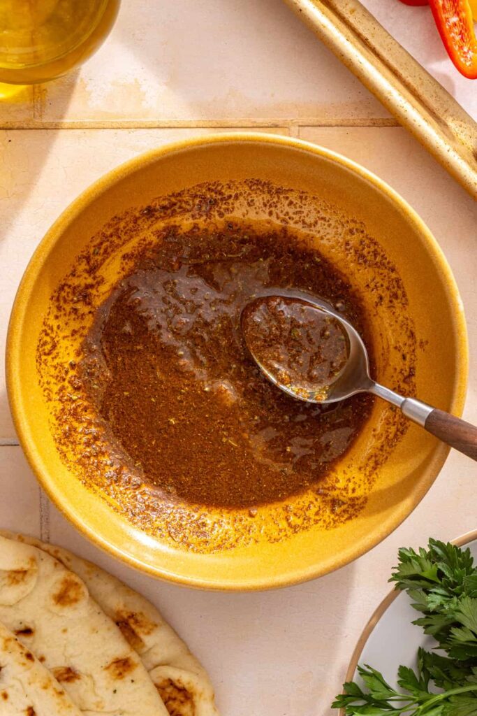 Homemade chicken shawarma marinade with olive oil, fresh lemon juice, minced garlic, and warm spices in a small bowl.