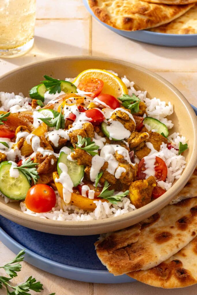 Chicken shawarma bowl topped with creamy feta sauce and parsley, showing layers of rice, roasted vegetables, and fresh toppings.