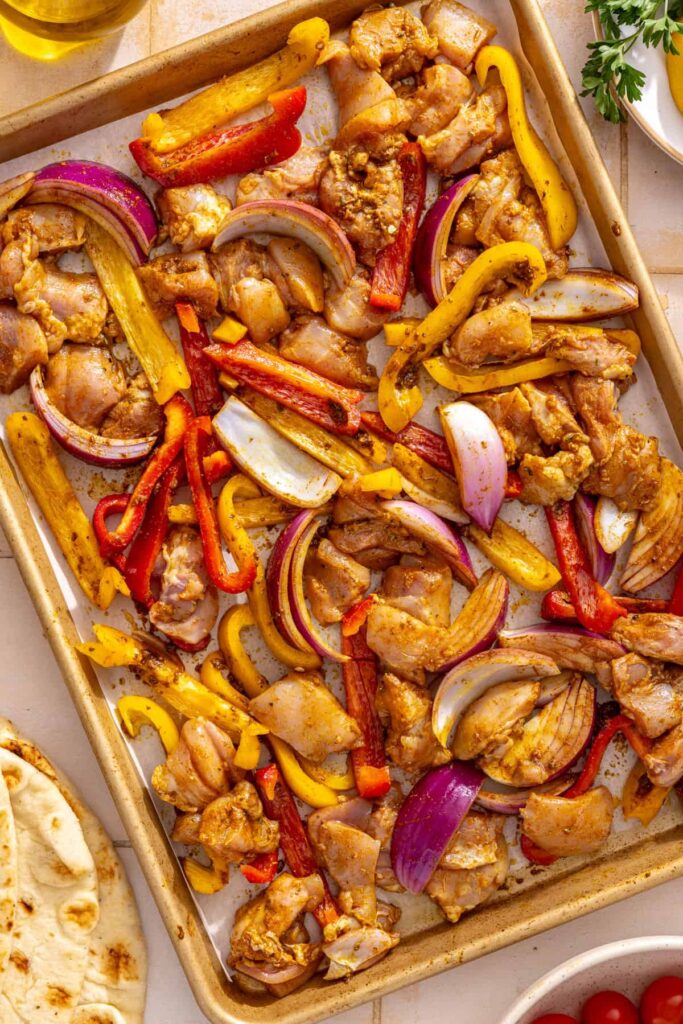 Chicken thighs, bell peppers, and red onion tossed with homemade shawarma seasoning on a sheet pan.