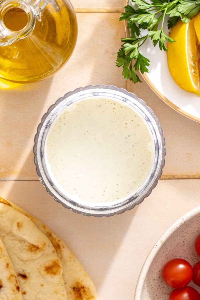Creamy feta garlic sauce blending in a food processor with feta cheese, Greek yogurt, garlic, and lemon.