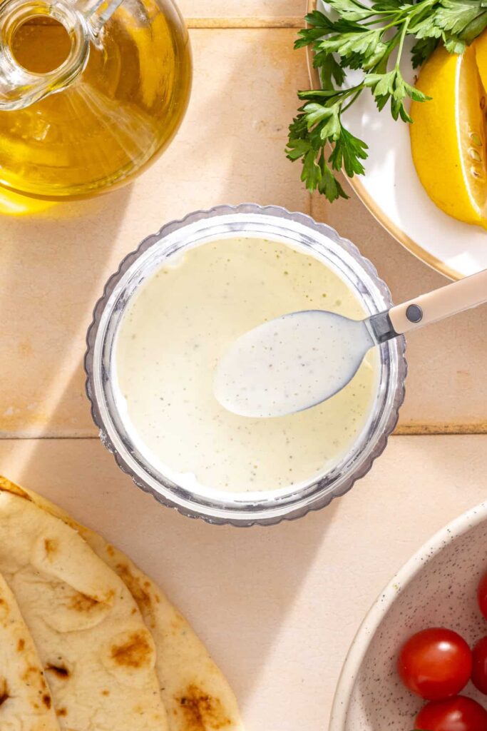 Thick feta garlic sauce being blended until creamy and easy to drizzle over chicken shawarma bowls.