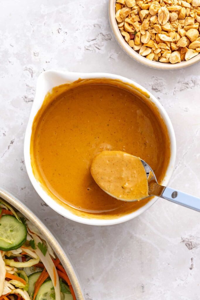 spoon lifting the whisked peanut butter, lime juice, coconut aminos, garlic, and ginger that made a creamy peanut sauce.