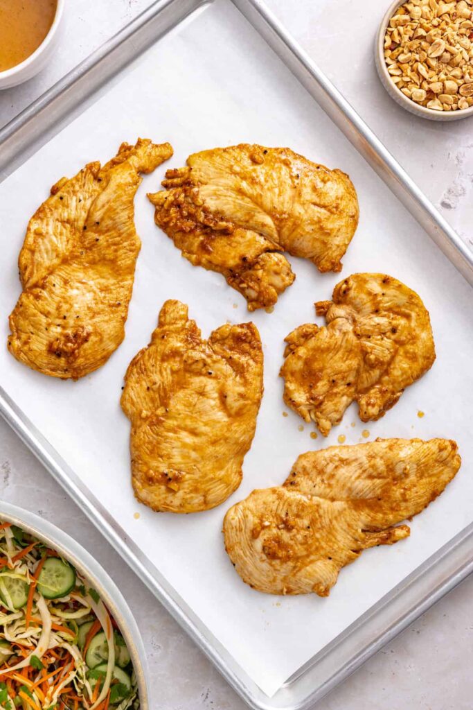 Oven-baked marinated chicken breasts resting on a parchment-lined baking sheet.