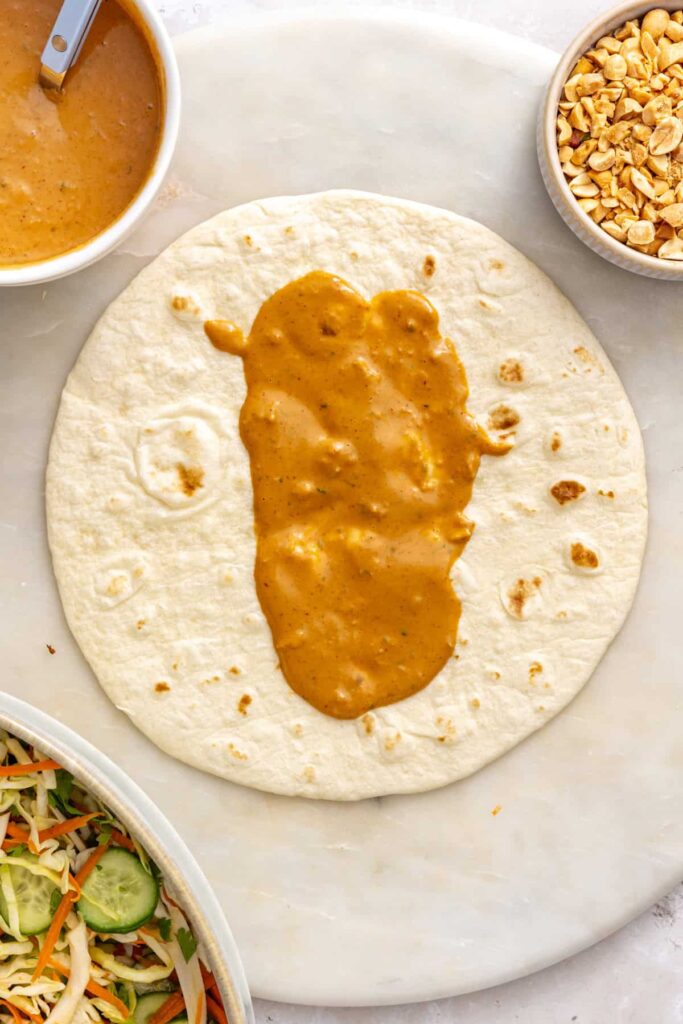 Creamy homemade peanut sauce spread down the center of a soft tortilla for a Thai peanut chicken wrap.