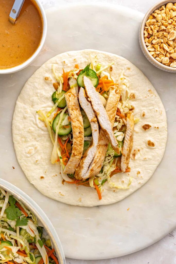 Sliced marinated chicken breast layered over crunchy vegetable slaw and peanut sauce in a tortilla.