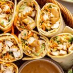 Overhead close-up of Thai peanut chicken wraps sliced in half and arranged upright on a serving platter with creamy peanut dipping sauce.