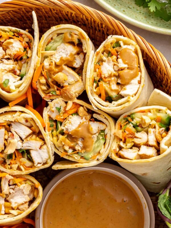 Overhead close-up of Thai peanut chicken wraps sliced in half and arranged upright on a serving platter with creamy peanut dipping sauce.
