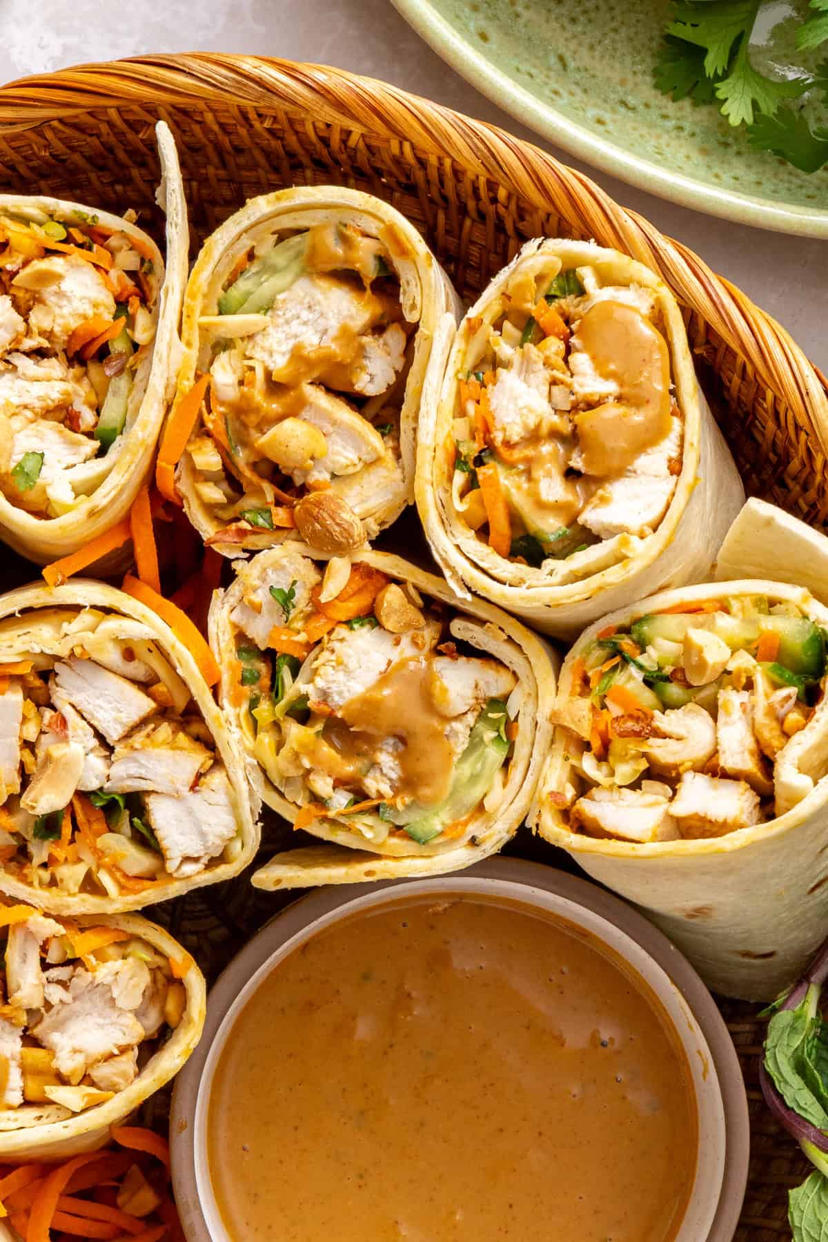 Overhead close-up of Thai peanut chicken wraps sliced in half and arranged upright on a serving platter with creamy peanut dipping sauce.