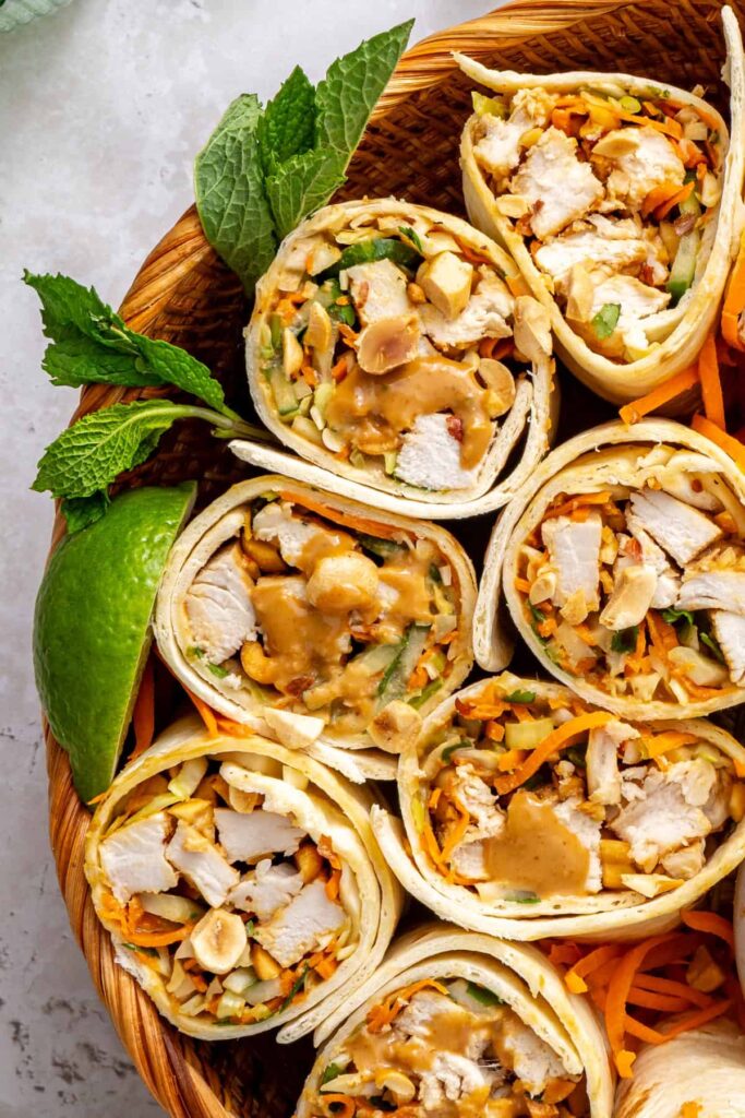 Overhead close-up of sliced Thai peanut chicken wraps on a serving platter, highlighting the colorful filling and soft tortilla.