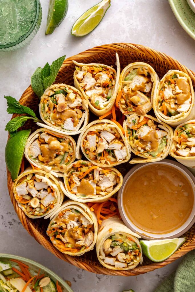 Close-up of the cut ends of Thai peanut chicken wraps beside creamy peanut dipping sauce on a serving platter.