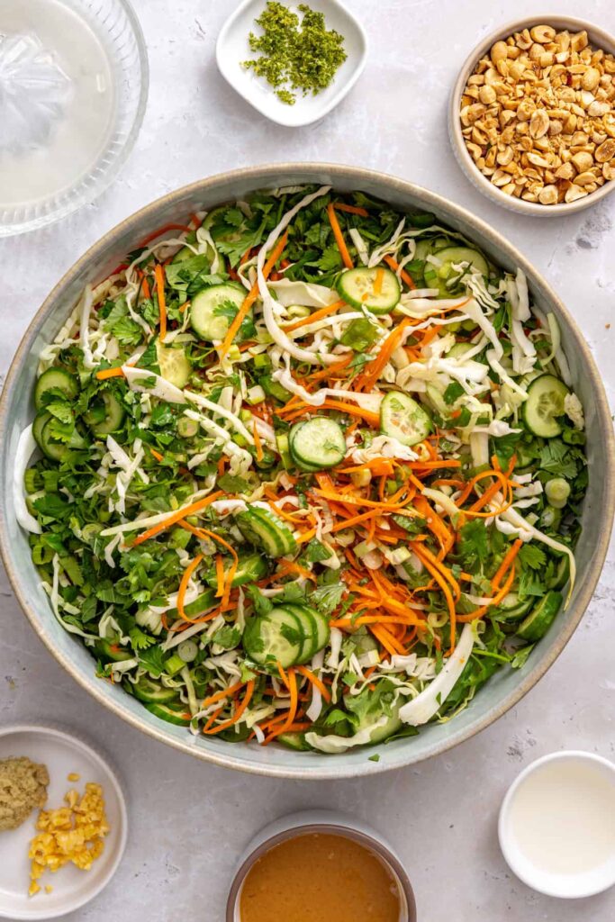 Shredded cabbage, carrots, sliced cucumbers, scallions, cilantro, and fresh mint in a bowl for crunchy Thai slaw.